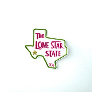 May include: Green outline of the state of Texas with the words "The Lone Star State" and "TX" inside. A gold star is in the centre of the outline.