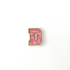 May include: Pink felt letter D with a gold outline. The letter is a classic style with a slightly rounded font.