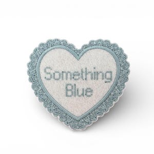 May include: A heart-shaped patch with the text "Something Blue" embroidered in light blue. The patch has a white centre and a light blue scalloped border. The patch is likely for a wedding or bridal theme.