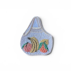 May include: A light blue embroidered patch shaped like a grocery bag with a white border. The design features a cluster of embroidered fruit including a pink peach, yellow bananas, and an orange citrus fruit with green leaves at the base.