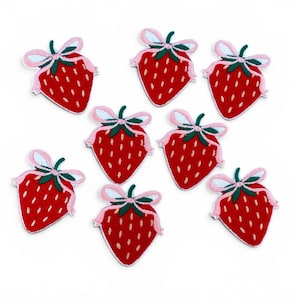 May include: A collection of eight embroidered strawberry patches. Each patch features a red strawberry with white seed details, a green stem, and a light pink ribbon tied in a bow at the top. The patches are arranged in a scattered pattern.