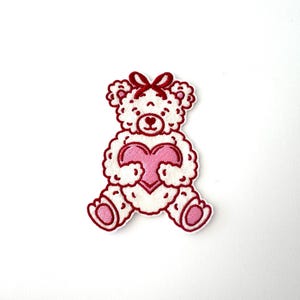 May include: White teddy bear holding a pink heart in its paws. The bear has a red bow on its head and is outlined in red.