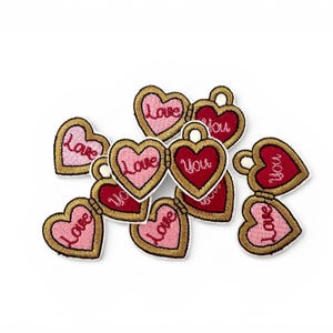 May include: Heart-shaped embroidered patches with gold edging, featuring the words "Love" and "You" in red and pink. The patches are scattered on a white background, suitable for Valentine's Day or craft activities.
