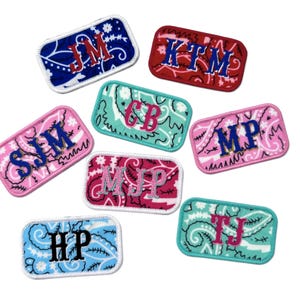 May include: A collection of rectangular patches with embroidered initials. The patches display a paisley pattern in blue, red, pink, and turquoise. Each patch has a white border and a unique set of initials.
