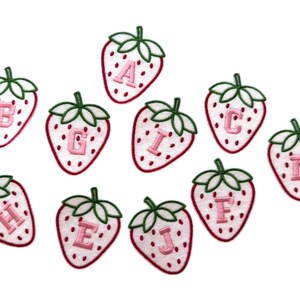 May include: Ten strawberry-shaped embroidered patches, each featuring a different letter. The strawberries are white with red outlines and green leaves. Ideal for customising clothing.