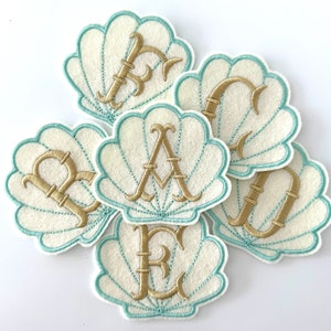 May include: Five white felt seashells with a teal blue outline. Each shell has a gold embroidered letter, spelling out the word "BREAD".