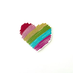 May include: A rainbow heart-shaped patch with a glittery finish. The heart is made of five different colours: red, pink, gold, green, and blue.