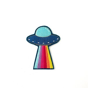 May include: An embroidered patch of a UFO with a rainbow beam of light coming out of the bottom, in blue and white.