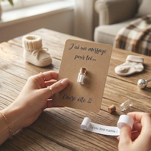 May include: A rectangular kraft paper card with the black printed text J'ai un message pour toi... and Ouvre vite !!!. A small glass bottle with a cork stopper is attached to the center. A white paper scroll with the text Tu vas &ecirc;tre mamie ! is shown.