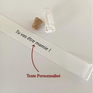 May include: A small clear glass vial with a separate cork stopper and a long white paper strip featuring the black printed text Tu vas &ecirc;tre mamie ! and a red arrow pointing to the text with the red label Texte Personnalis&eacute; below it.