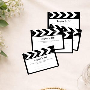 Peut inclure: Plusieurs cartes blanches avec un motif de clapperboard noir. Les cartes comportent le texte "Inspire le DJ" et du texte supplémentaire en français. Les clapperboards sont disposés en chevauchement.