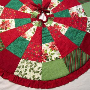 May include: A circular Christmas tree skirt featuring a patchwork design of red, dark green, and light green fabric panels. The pattern includes poinsettia flowers, holly leaves, and striped motifs. The edge is finished with a red fabric ruffle.