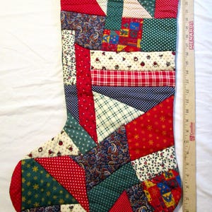 May include: A patchwork Christmas stocking made of various fabric scraps in red, green, blue, and cream with diverse patterns including polka dots, plaid, and paisley. A wooden ruler is placed alongside, showing a length of approximately 27 inches.