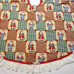 May include: A circular Christmas tree skirt featuring a patchwork design of alternating squares. The fabric squares display repeating illustrations of Santa Claus, red and white polka dots, and a green plaid pattern. A red trim and white lace border.