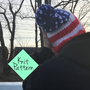 May include: Knit hat with a red, white, and blue striped pattern and a blue pom pom. The hat is made with a knit stitch and has a star pattern on the pom pom. The hat is being worn by a person.