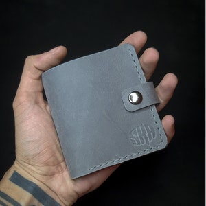 May include: A gray leather wallet with a snap closure and a monogrammed design.