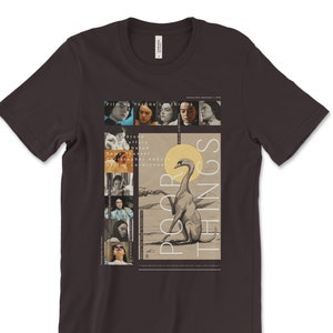 May include: A dark gray t-shirt with a graphic design featuring a collage of images from the film "Poor Things". The film title is printed in white letters on a black background. The graphic design includes a swan, a dog, and several portraits of actors from the film.