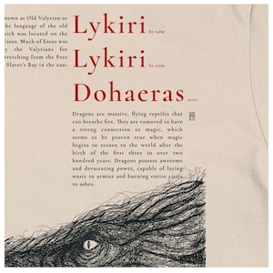 May include: Cream-coloured t-shirt with red text: "Lykiri be calm" and "Dohaeras serve." A black and white illustration of a dragon's eye and scales is below the text. The shirt also has text about dragons.