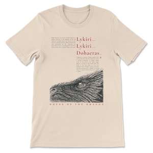 May include: Beige t-shirt with a black and white dragon illustration and text. The text includes "Lykiri", "Dohaeras", and "House of the Dragon". The shirt is made of a soft material.