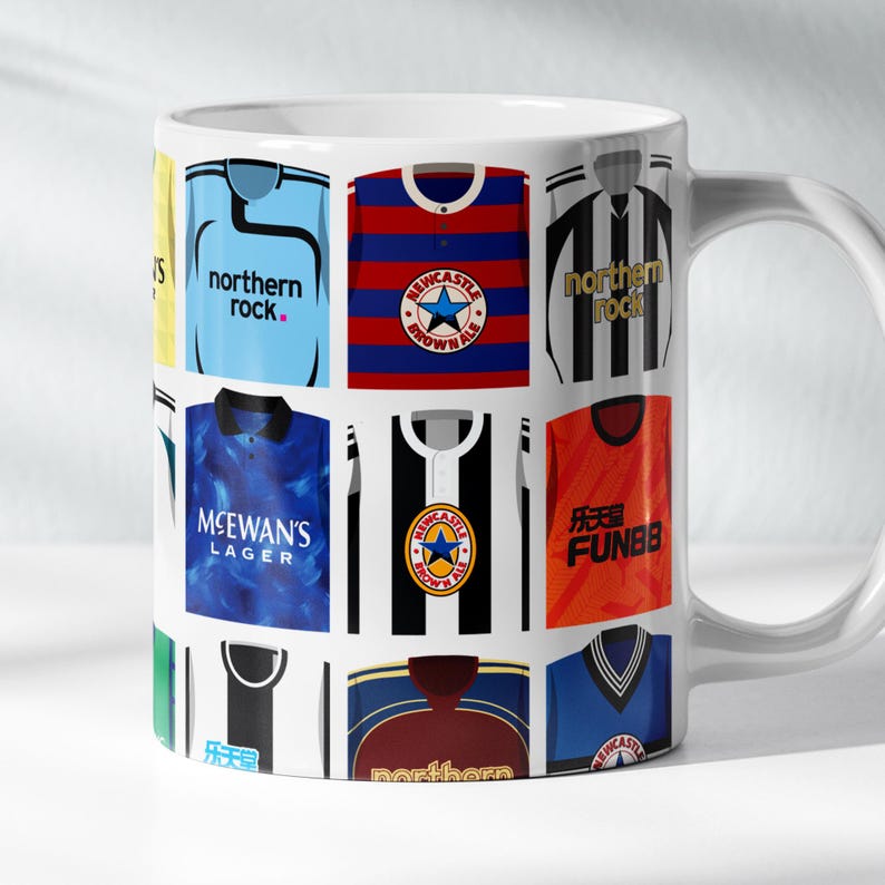 May include: White ceramic mug with a pattern of different soccer jerseys. The jerseys feature various colors, logos, and sponsors, including "northern rock", "MCEWAN'S LAGER", and "FUNBB".