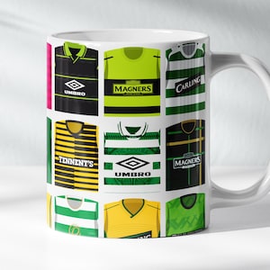 May include: White ceramic mug decorated with a collage of football shirts in green, yellow, and black. The shirts feature logos and text, including "Umbro", "Tennent's", and "Magners".