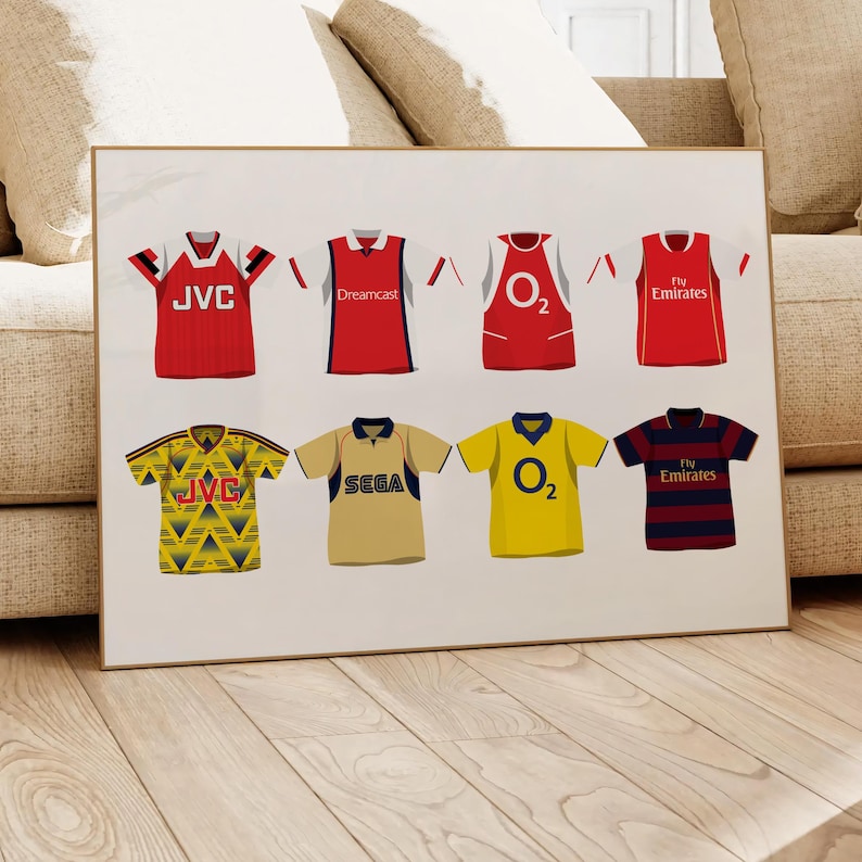 May include: A white background with a collage of eight different Arsenal football jerseys. The jerseys feature various sponsors including JVC, Dreamcast, O2, and Fly Emirates. The jerseys are in red, yellow, blue, and white.