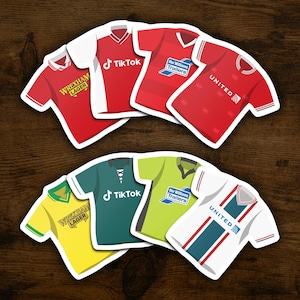 以下が含まれることがあります： サッカーのジャージーステッカーの異なるデザインが8つあります。ジャージは赤、緑、黄、白で、TikTok、Ifor Williams Trailers、Wrexham Lagerなど、さまざまなスポンサーがいます。