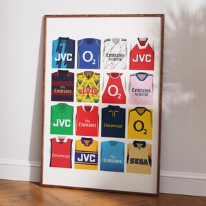 May include: A poster featuring a collage of 16 different soccer jerseys, each with a different sponsor logo. The sponsors include JVC, O2, Emirates, Dreamcast, and Sega. The jerseys are in various colors, including red, blue, yellow, green, and white.