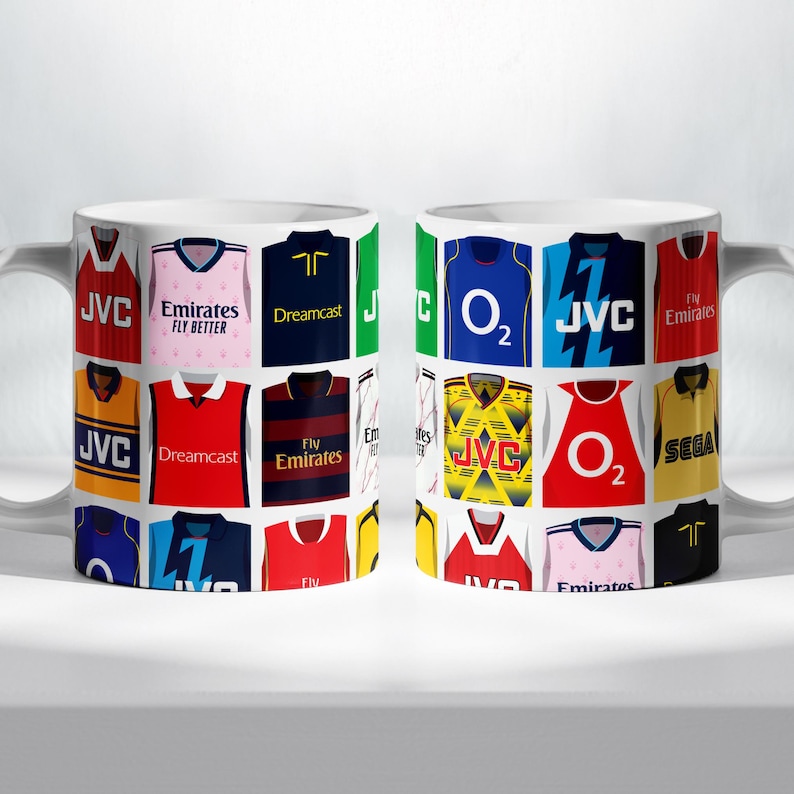 May include: Two white mugs with a collage of different soccer jerseys printed on them. The jerseys feature various sponsors like JVC, Emirates, Dreamcast, O2, and Sega.