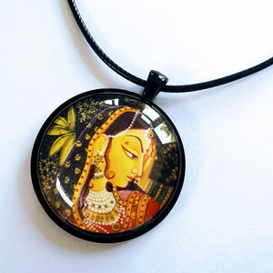 May include: A round glass pendant necklace with a black cord. The pendant features a colorful illustration of a woman in traditional Indian clothing.