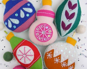 May include: Six felt Christmas ornaments in various colors and designs. The ornaments are decorated with sequins and embroidery. The ornaments are arranged on a white surface with colorful confetti.
