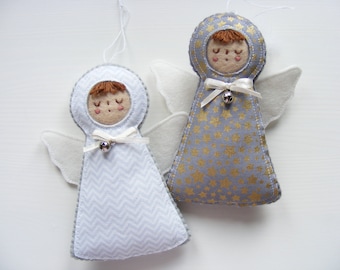 May include: Two handmade felt angel ornaments with white wings. One angel is white with a chevron pattern and the other is gray with gold stars. Both angels have brown hair, closed eyes, and a small bell.