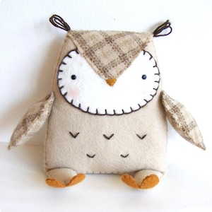 May include: A brown and white felt owl with a plaid pattern on its head. The owl has black eyes, a brown beak, and brown felt feet.