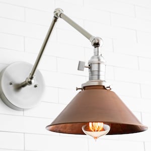 May include: A wall-mounted, adjustable lamp with a brushed nickel finish. The lamp features a conical, copper-colored shade and an exposed Edison-style bulb. The fixture is mounted on a white tiled wall, showcasing a modern, industrial design.