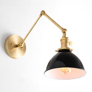 May include: A black and gold wall sconce with an adjustable arm. The sconce has a black metal shade with a white interior and a gold metal base.