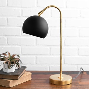 May include: A gold desk lamp with a black spherical shade. The lamp is on a wooden table with a small potted plant.
