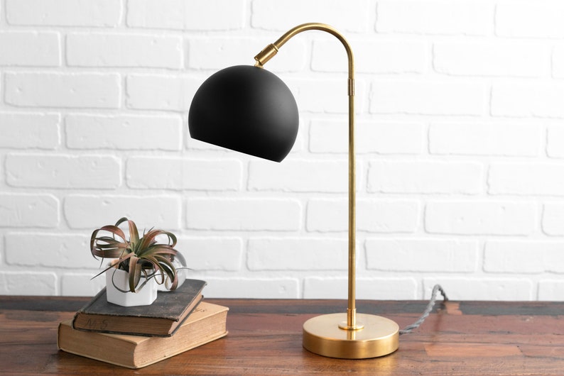 May include: A gold desk lamp with a black spherical shade. The lamp is on a wooden table with a small potted plant.