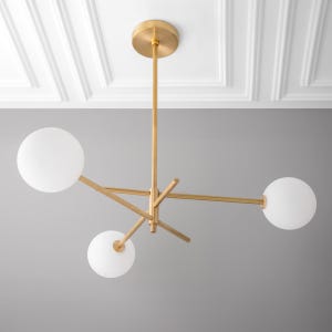 May include: A gold modern chandelier with three white globe-shaped light bulbs. The chandelier has a geometric design with three arms extending from a central rod.
