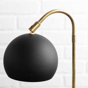 May include: A black globe lampshade with a gold metal arm and base.