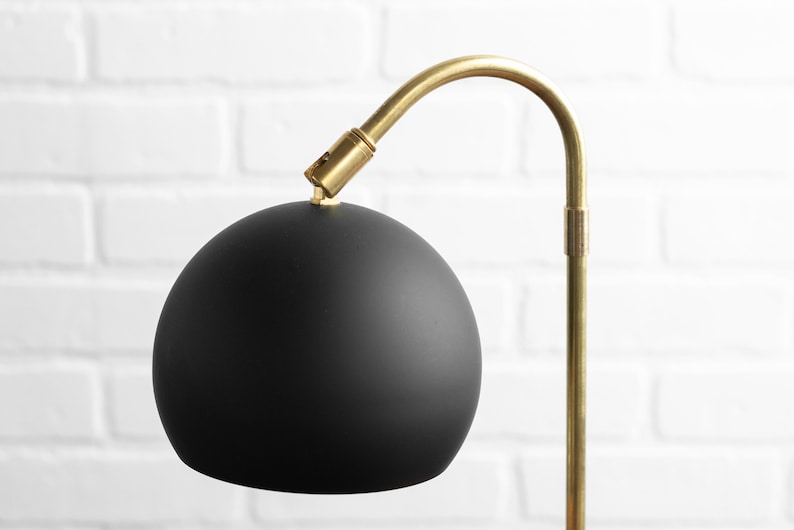May include: A black globe lampshade with a gold metal arm and base.
