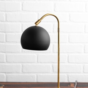 May include: A black and gold table lamp with a curved arm and a round black shade. The lamp is on a wooden surface.