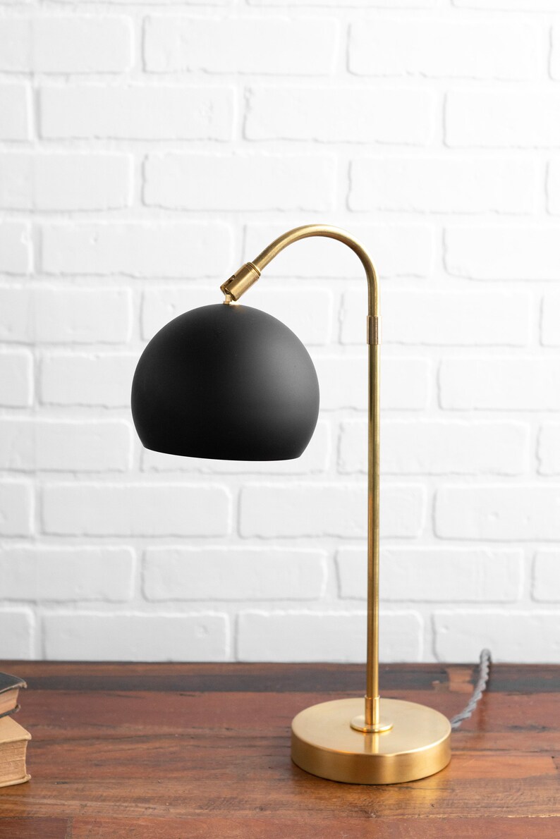 May include: A black and gold table lamp with a curved arm and a round black shade. The lamp is on a wooden surface.