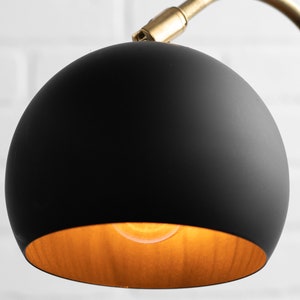 May include: A black globe lampshade with a gold interior. The lampshade is attached to a gold metal arm.