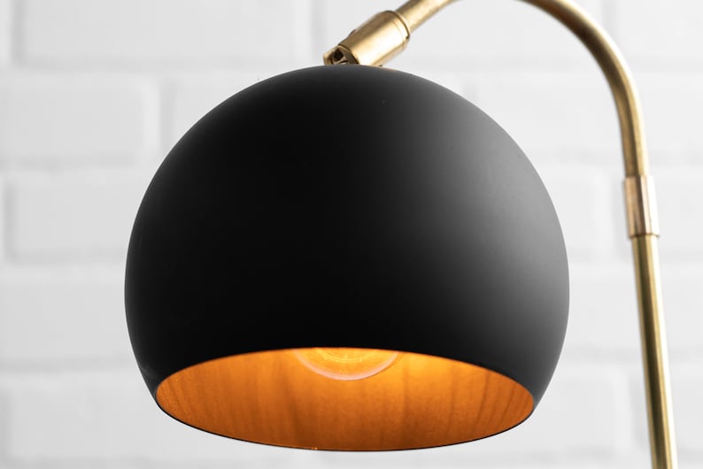 May include: A black globe lampshade with a gold interior. The lampshade is attached to a gold metal arm.