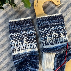 Könnte beinhalten: Ein Paar blaue und weiße Stricksocken mit einem Schneeflockenmuster. Die Socken hängen an einem Holzaufhänger mit dem Text "From Devon With Love".