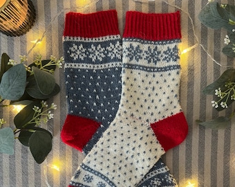 Peut inclure: Une paire de chaussettes tricotées avec un motif de flocon de neige blanc et bleu et des revers rouges. Les chaussettes sont sur un fond de tissu rayé.