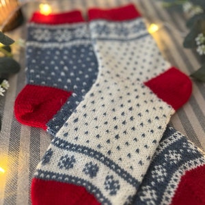 May include: A pair of knitted socks with a white, blue and red snowflake pattern. The socks are folded together and have a red cuff.