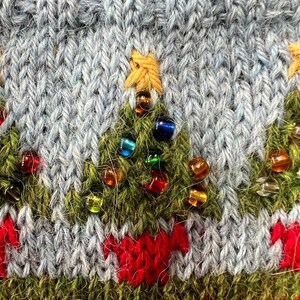 Peut inclure: Gros plan sur un motif de No&euml;l tricot&eacute;. Le tissu en tricot bleu clair pr&eacute;sente des sapins de No&euml;l verts brod&eacute;s orn&eacute;s de perles color&eacute;es. Un motif rouge et blanc se trouve en bas, et une &eacute;toile jaune surmonte chaque arbre.