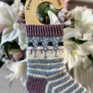 May include: A pair of striped socks with a purple cuff and a white and blue pattern. The socks are hanging on a wooden hanger with the text "From Devon With Love" engraved on it.