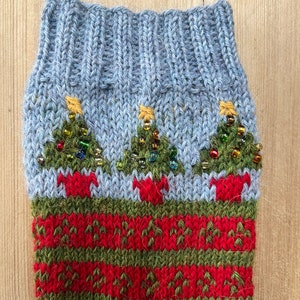 Peut inclure: Une chaussette de No&euml;l tricot&eacute;e avec un revers bleu clair et un corps &agrave; motifs rouges et verts. La chaussette pr&eacute;sente trois sapins de No&euml;l verts avec des &eacute;toiles dor&eacute;es et des ornements perl&eacute;s.